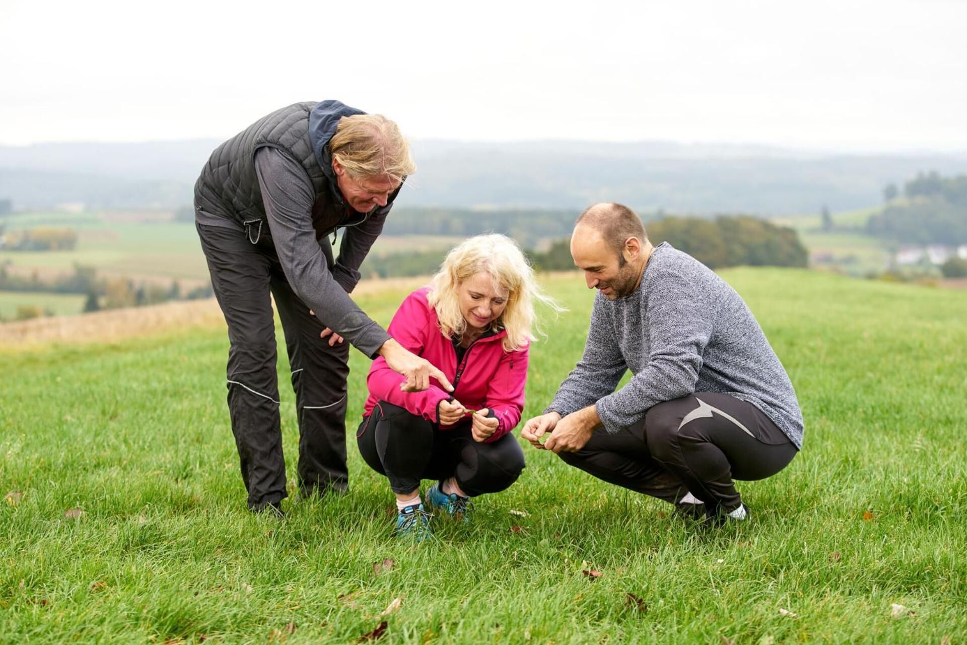 Three people in a grassy field with a hilly landscape in the background.