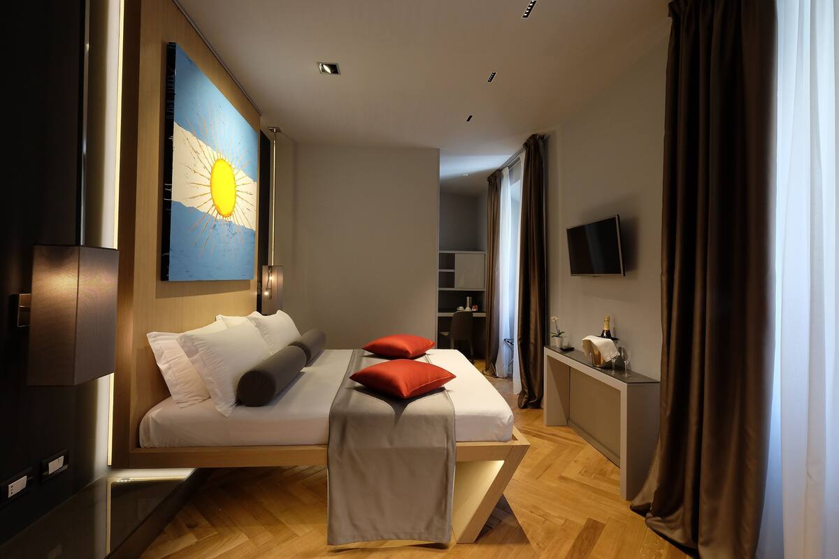 A modern hotel room with a bed, a desk, a TV, and a large window with curtains.