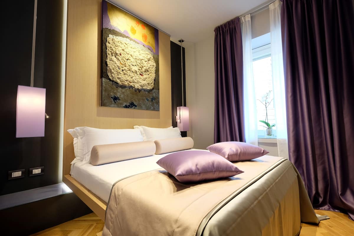 A modern hotel room with a large bed, a painting on the wall, and a window with curtains.
