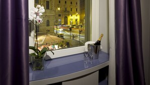 A hotel room with a window overlooking a city street at night, a vase with an orchid, and a bottle of champagne on the windowsill. - Navona Rooms (Rome)