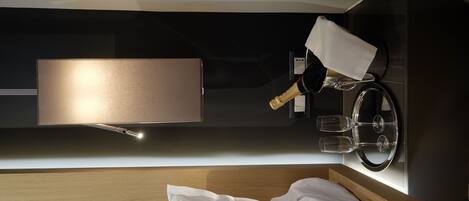 A modern hotel room with a wooden headboard, a wall-mounted wine glass holder, and a large mirror.