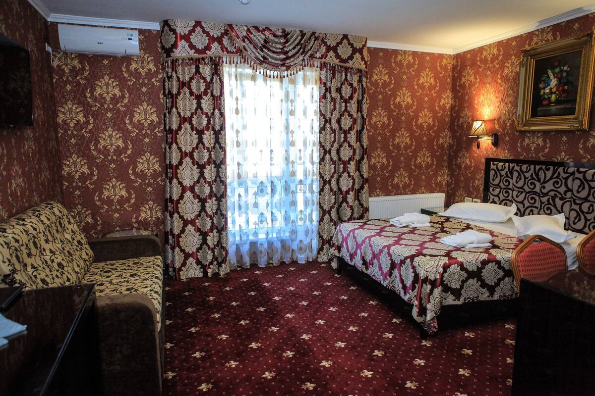 A hotel room with a bed, a sofa, a desk, and a wall-mounted TV.