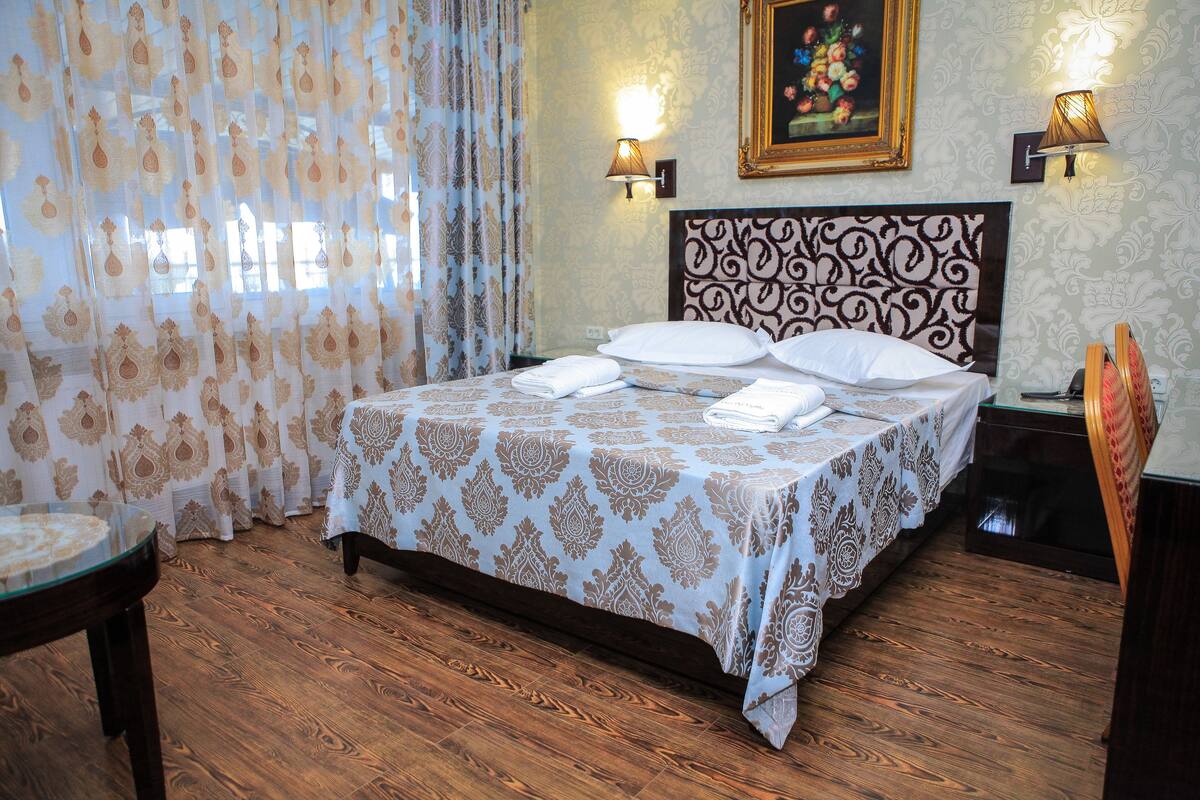 A neatly made bed with a patterned bedspread, two wall-mounted lamps, and a framed picture on the wall.