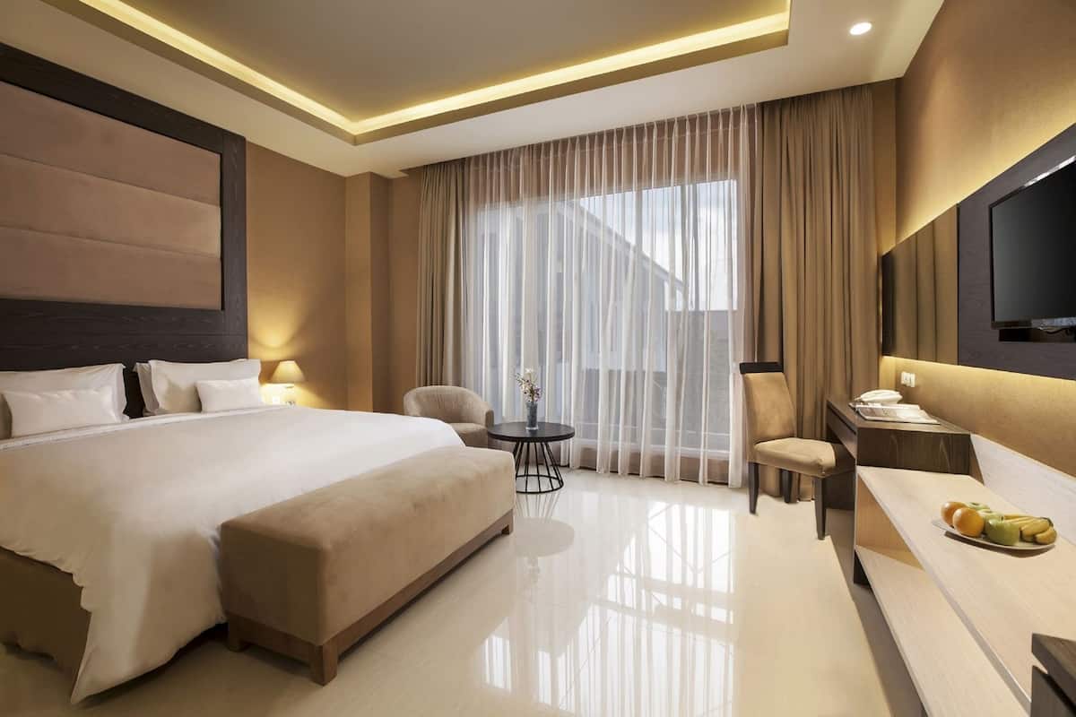 Ein Hotelzimmer mit einem großen Bett, einem Schreibtisch mit Stuhl, einem kleinen Tisch und einem Fernseher.