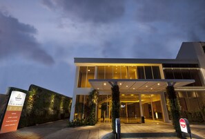 A modern hotel entrance with a glass facade, a reception area, and a landscaped entrance. - Lunara Home Living by Daphna Management (Yogyakarta)