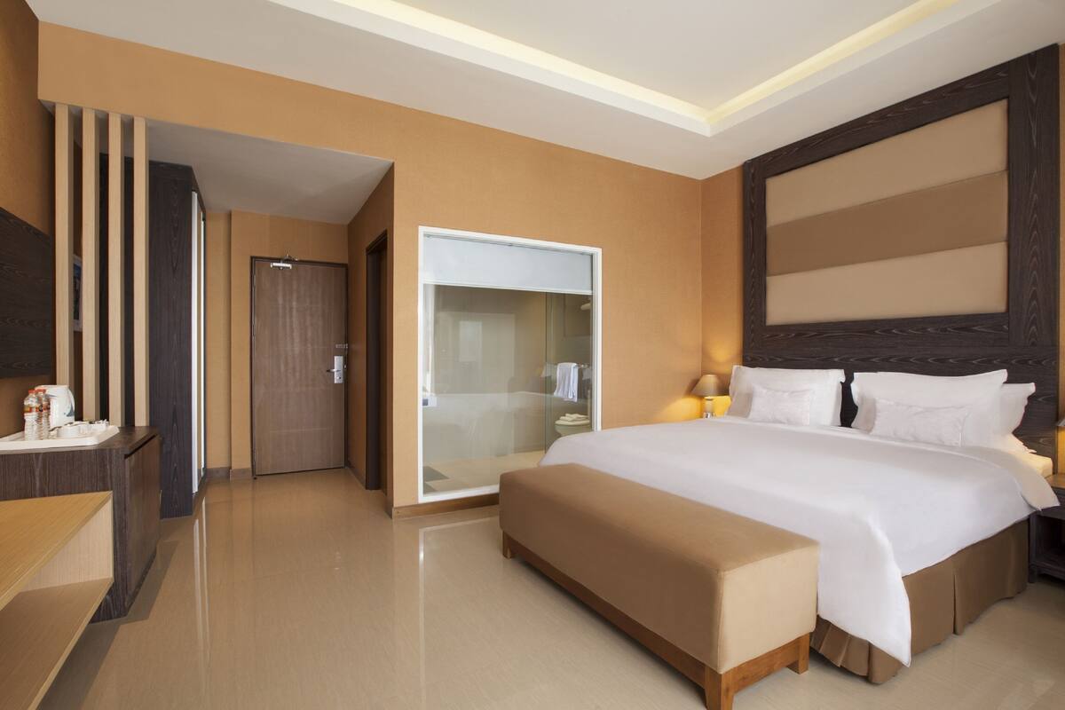 Ein modernes Hotelzimmer mit einem großen Bett, einem begehbaren Kleiderschrank und einem Badezimmer mit Duschkabine.