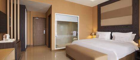Una habitación de hotel moderna con una cama grande, un vestidor y un baño con cabina de ducha de vidrio.