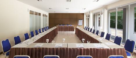 Une salle de conférence avec une longue table, des chaises bleues et une vue sur la verdure grâce à de grandes fenêtres.
