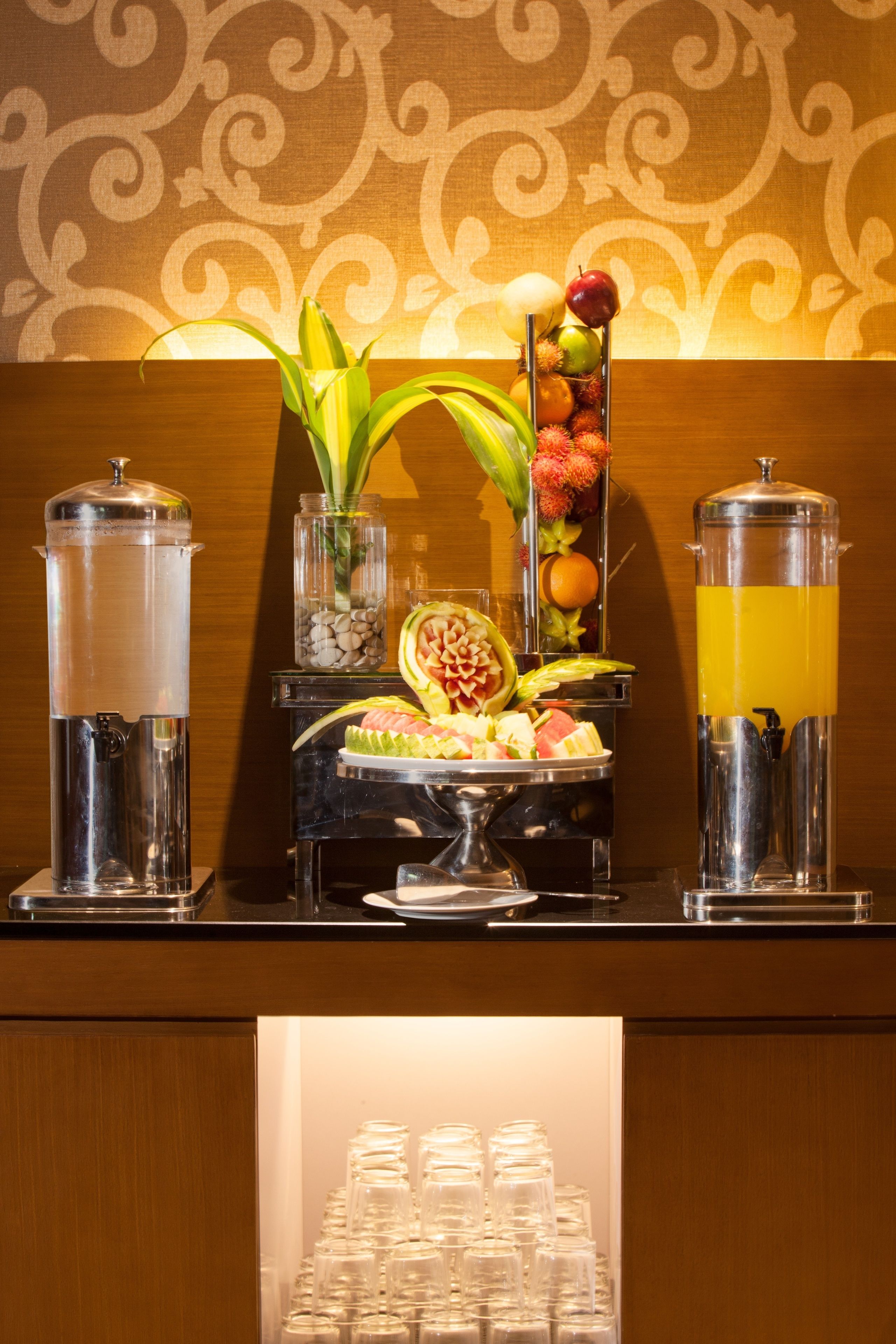 A buffet setup with a fruit display, a water dispenser, and a juice dispenser.