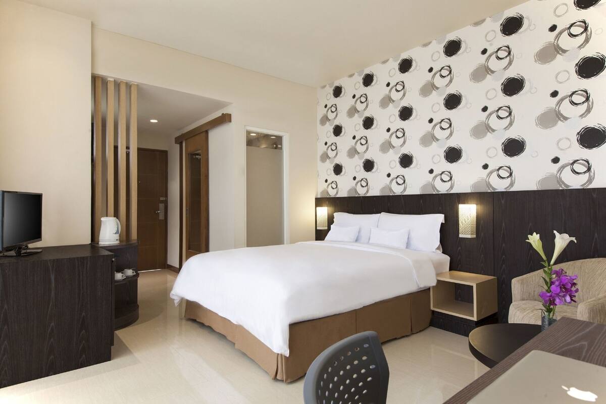 Ein Hotelzimmer mit einem großen Bett, einem Schreibtisch mit Computer, einem Sessel, einer Kaffeemaschine und einem Fernseher.
