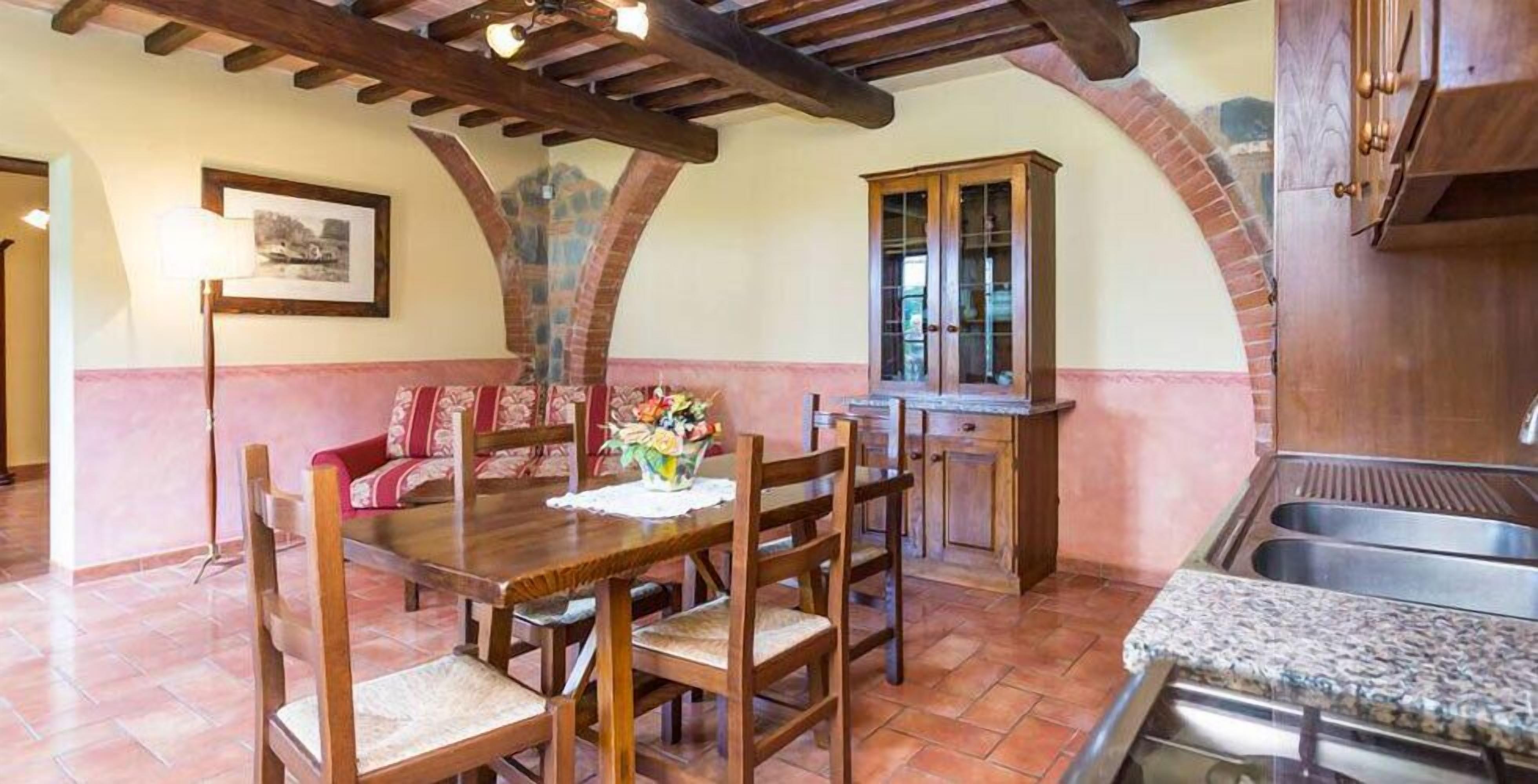 A dining area with a wooden table and chairs, a vase of flowers, and a brick archway.