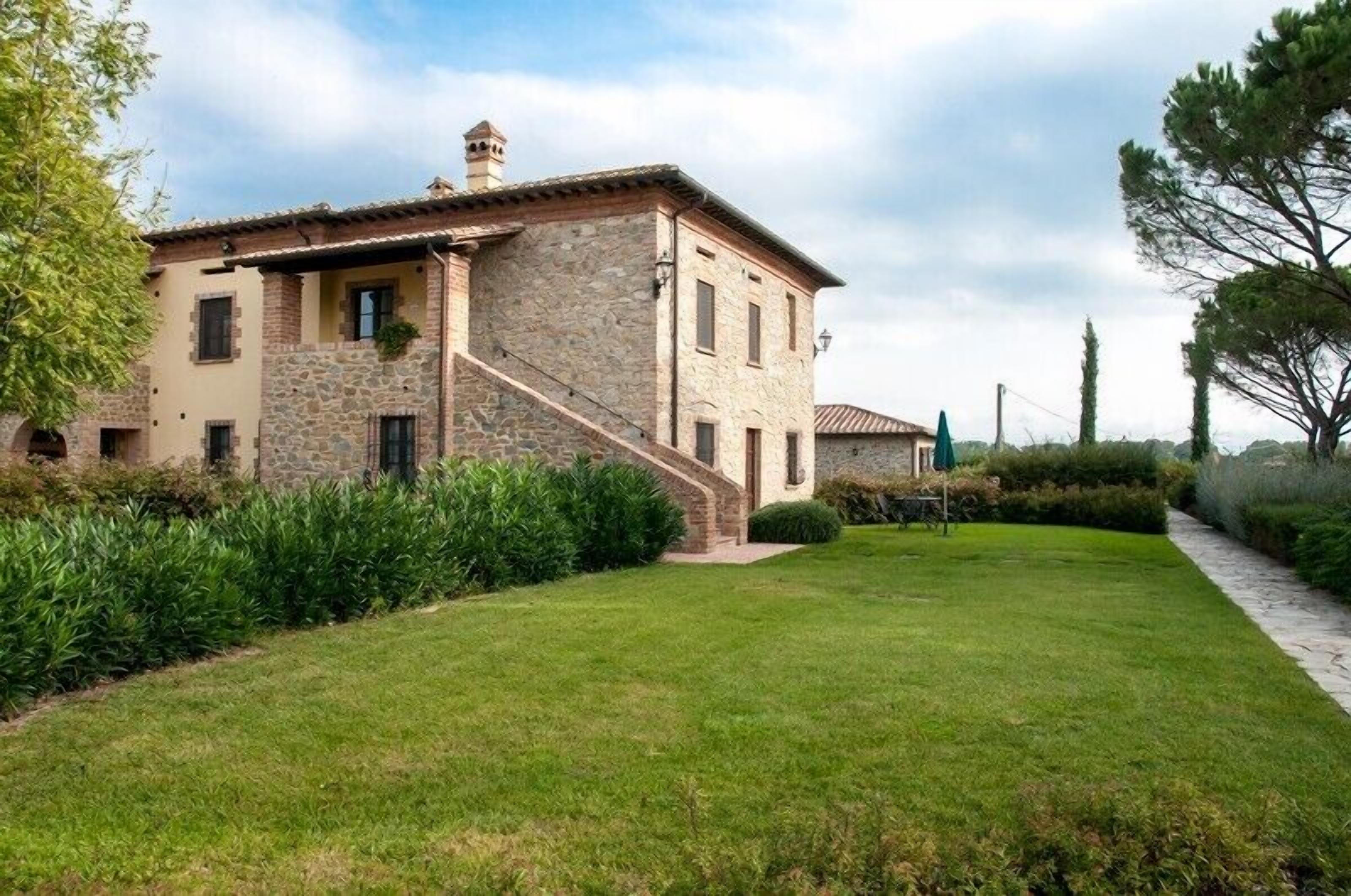 A stone building with a staircase leading to the entrance, surrounded by a well-maintained lawn and hedges.