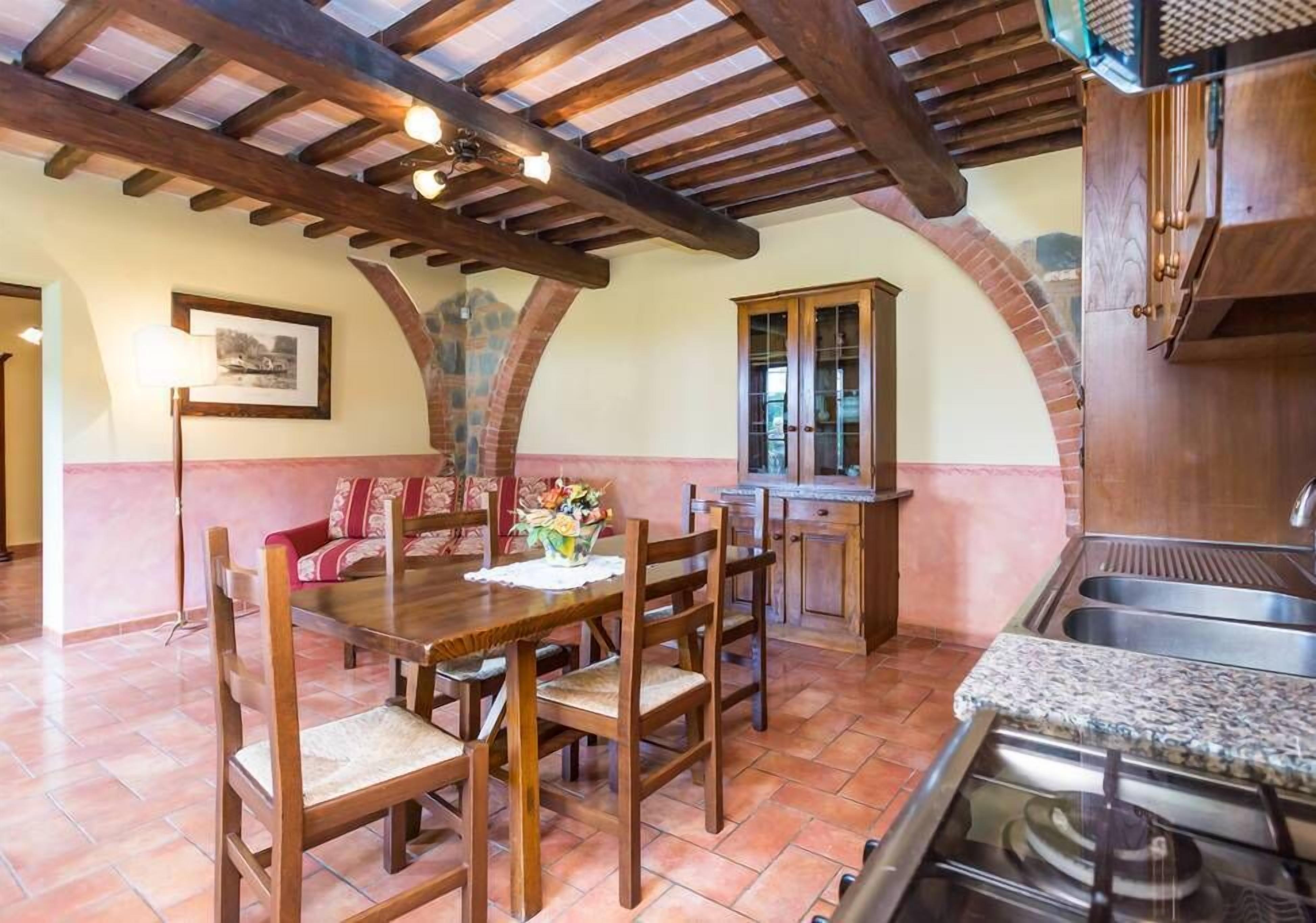 A dining area with a wooden table and chairs, a kitchen with a stove, and a stone archway.