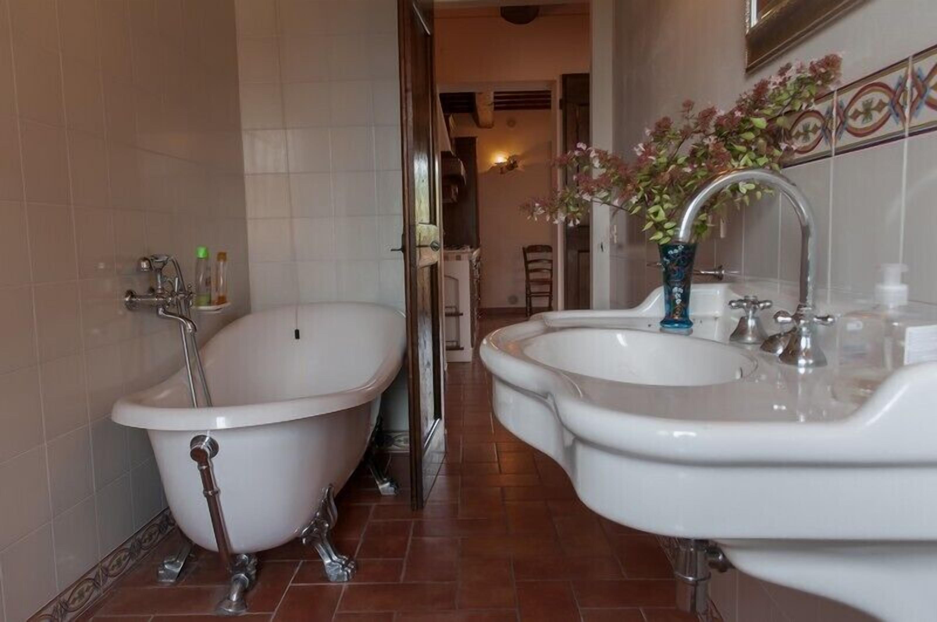 Un baño con dos tinas de patas de león, un lavamanos y un florero con flores.