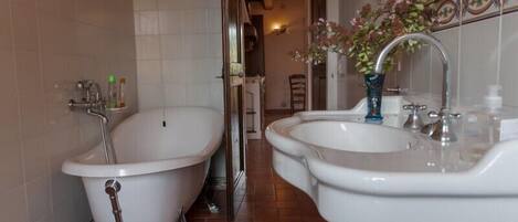 Un baño con dos tinas de patas de león, un lavamanos y un florero con flores.