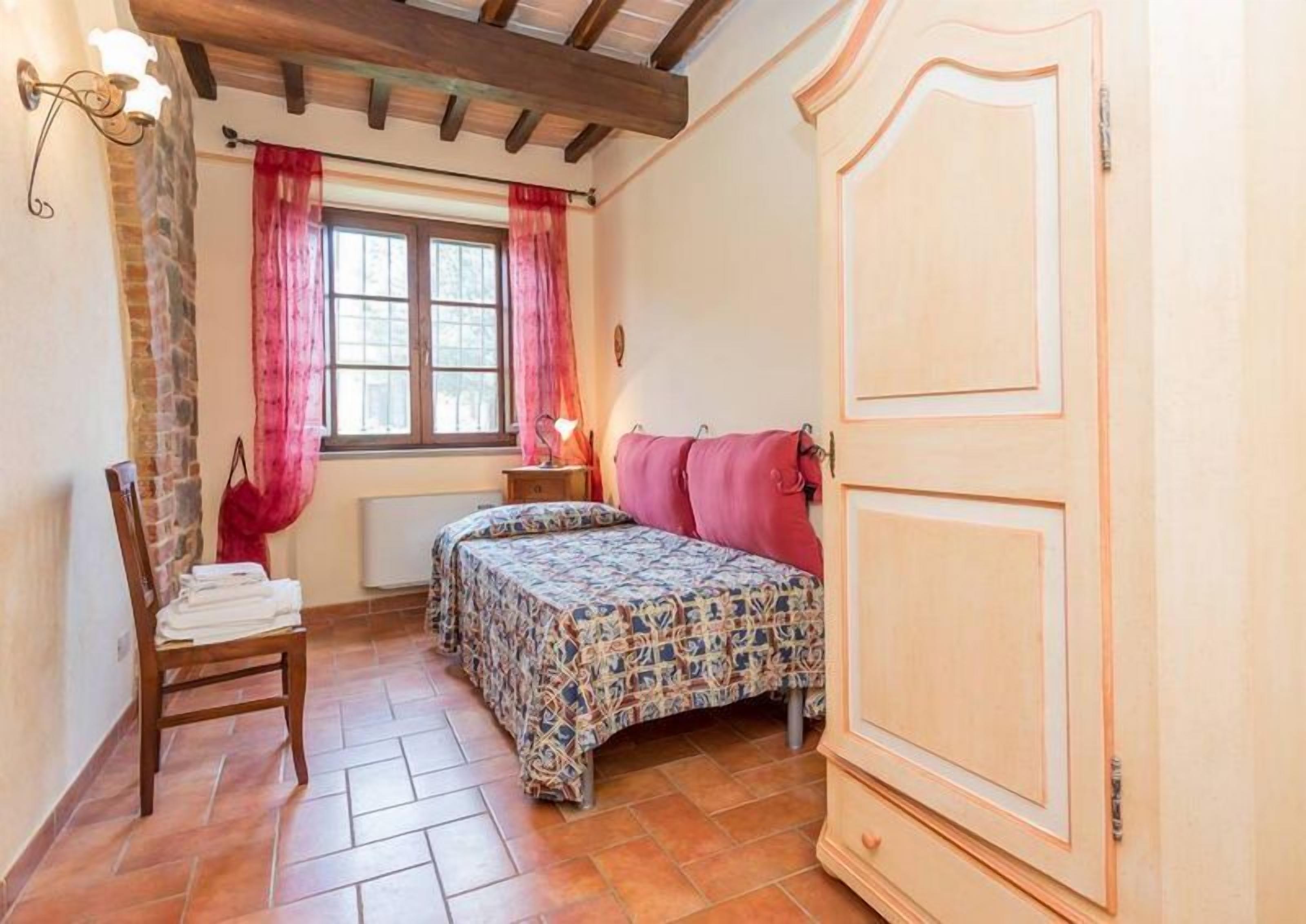 Une chambre à coucher avec un lit, une chaise, une fenêtre avec des rideaux, un radiateur et une armoire.