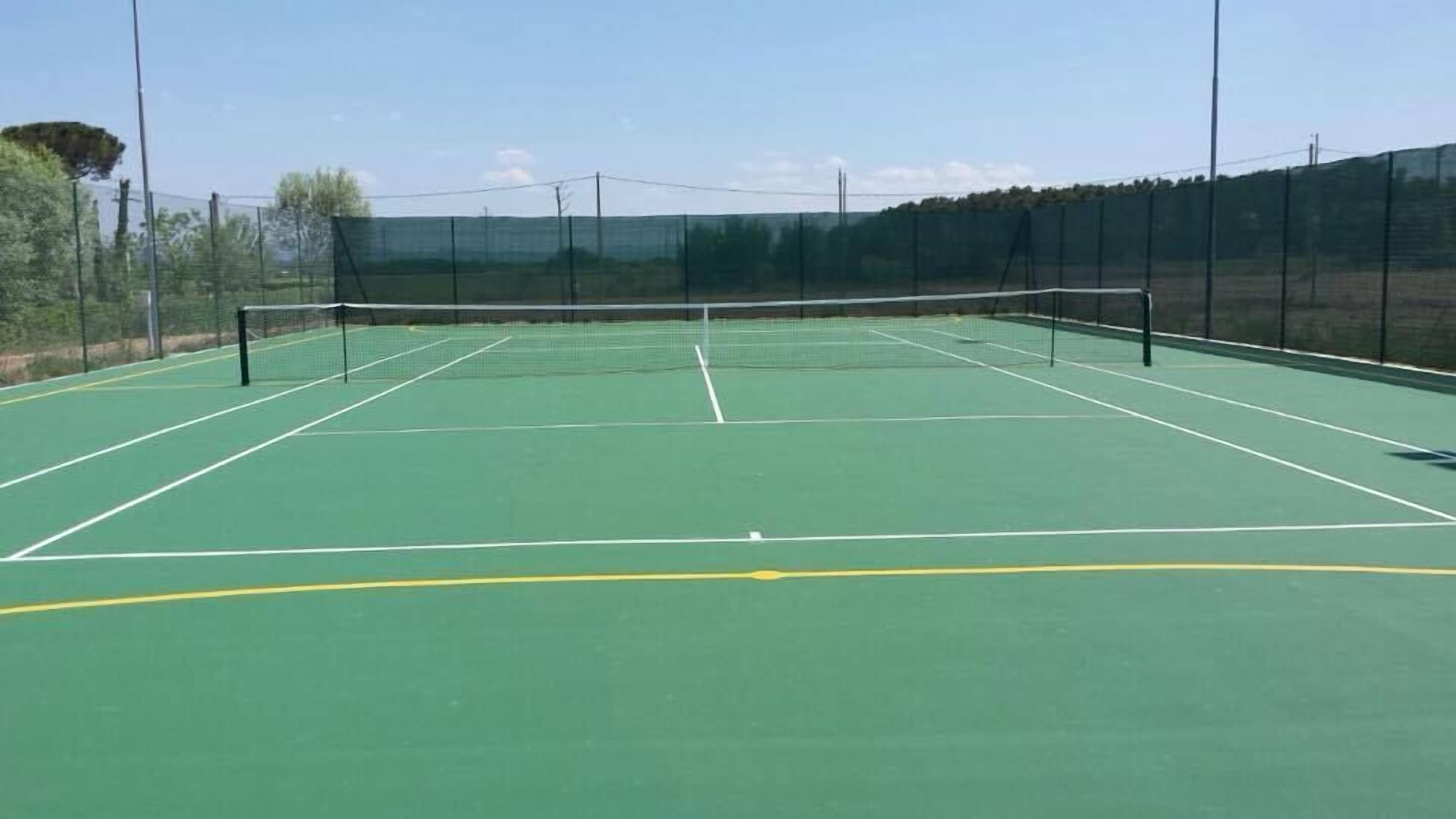 Un campo da tennis con una rete, circondato da una recinzione e alberi.