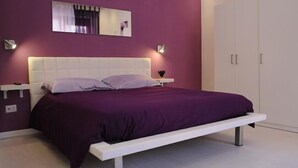 A bedroom with a bed, a nightstand, a wall-mounted light, and a wardrobe.