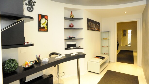 A modern, well-lit room with a curved ceiling, a black desk with a chair, a white sofa, and various decorative items on shelves.