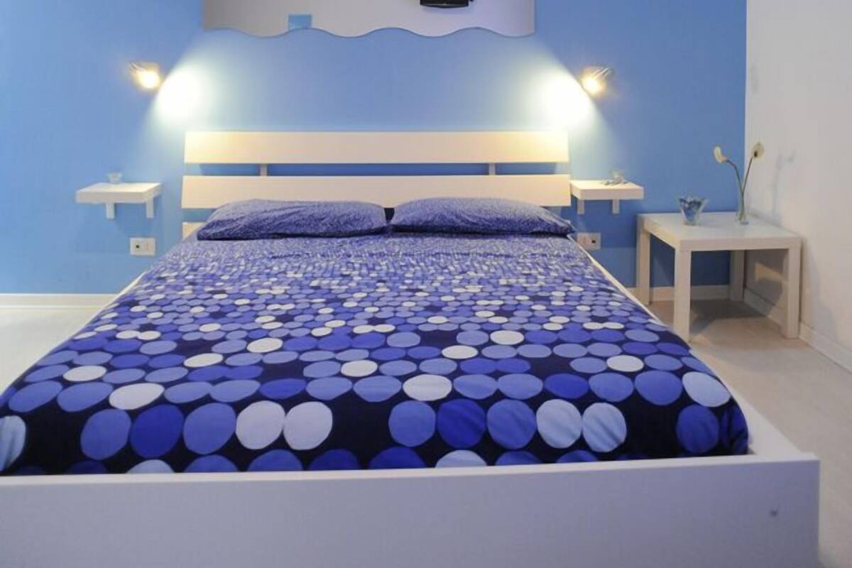 Un dormitorio con cama, mesitas de noche y una lámpara fijada a la pared.