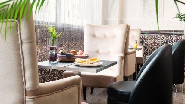 A dining area with a table set for two, featuring a variety of food items and a vase of flowers.