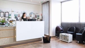 A reception area with a white desk, black chairs, a small white table, and a large window.