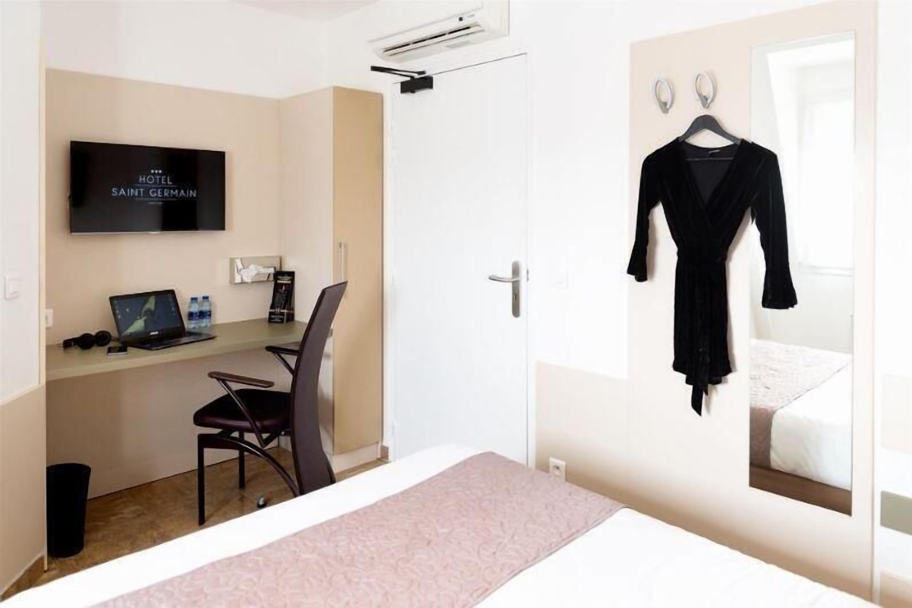 Habitación de hotel con cama, escritorio con computadora portátil, silla, televisor y bata negra colgada en la pared.