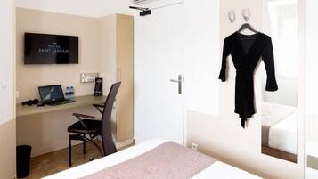 Habitación de hotel con cama, escritorio con computadora portátil, silla, televisor y bata negra colgada en la pared.
