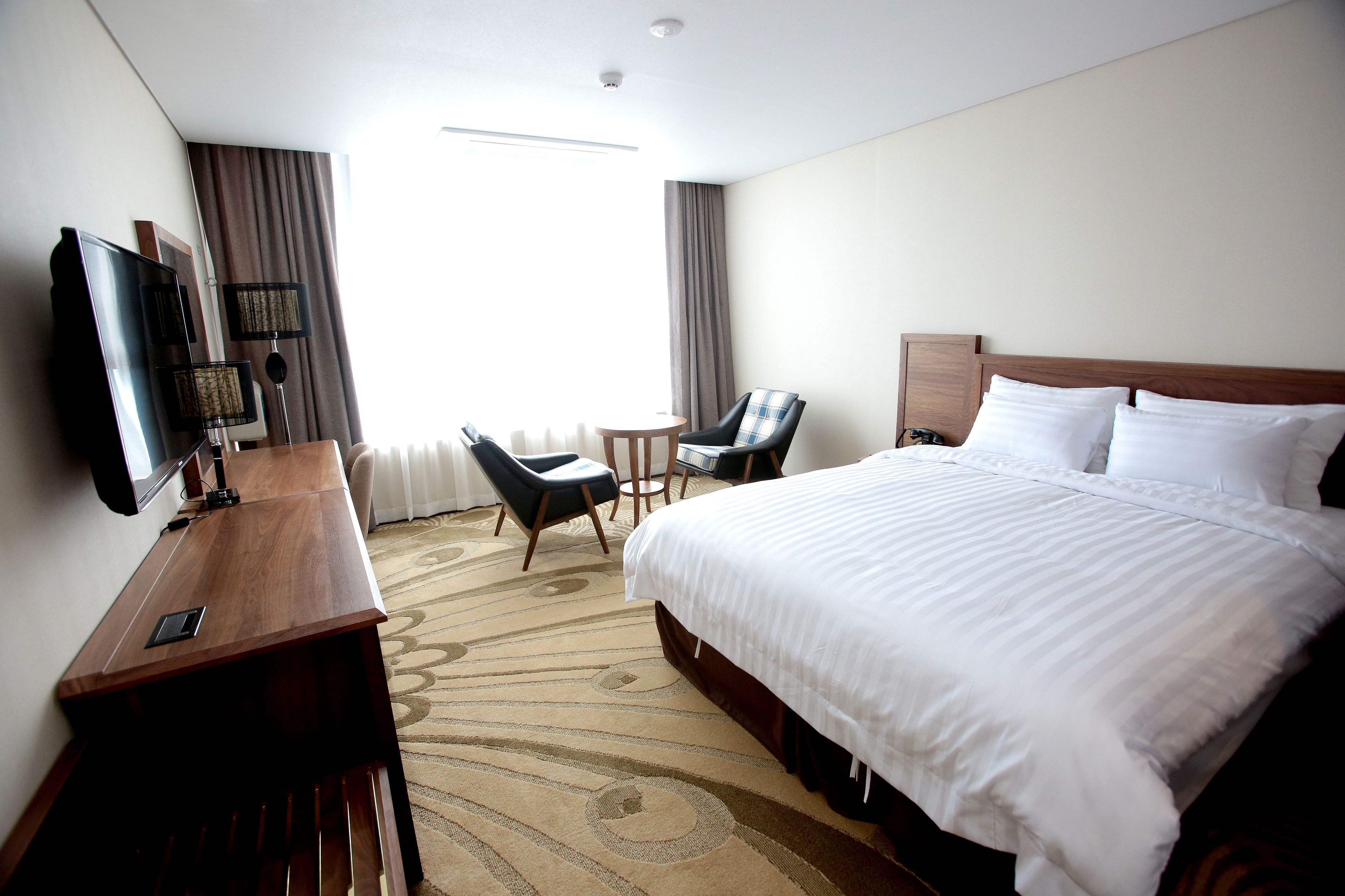 Une chambre d’hôtel avec un grand lit, un bureau doté d’un téléviseur à écran plat, une chaise et une petite table.