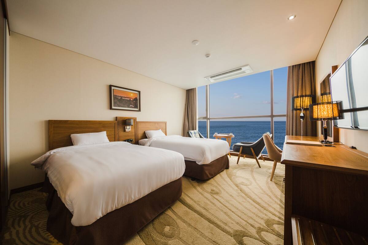 Ein Hotelzimmer mit zwei Betten, einem Schreibtisch, einem Stuhl und Meerblick.
