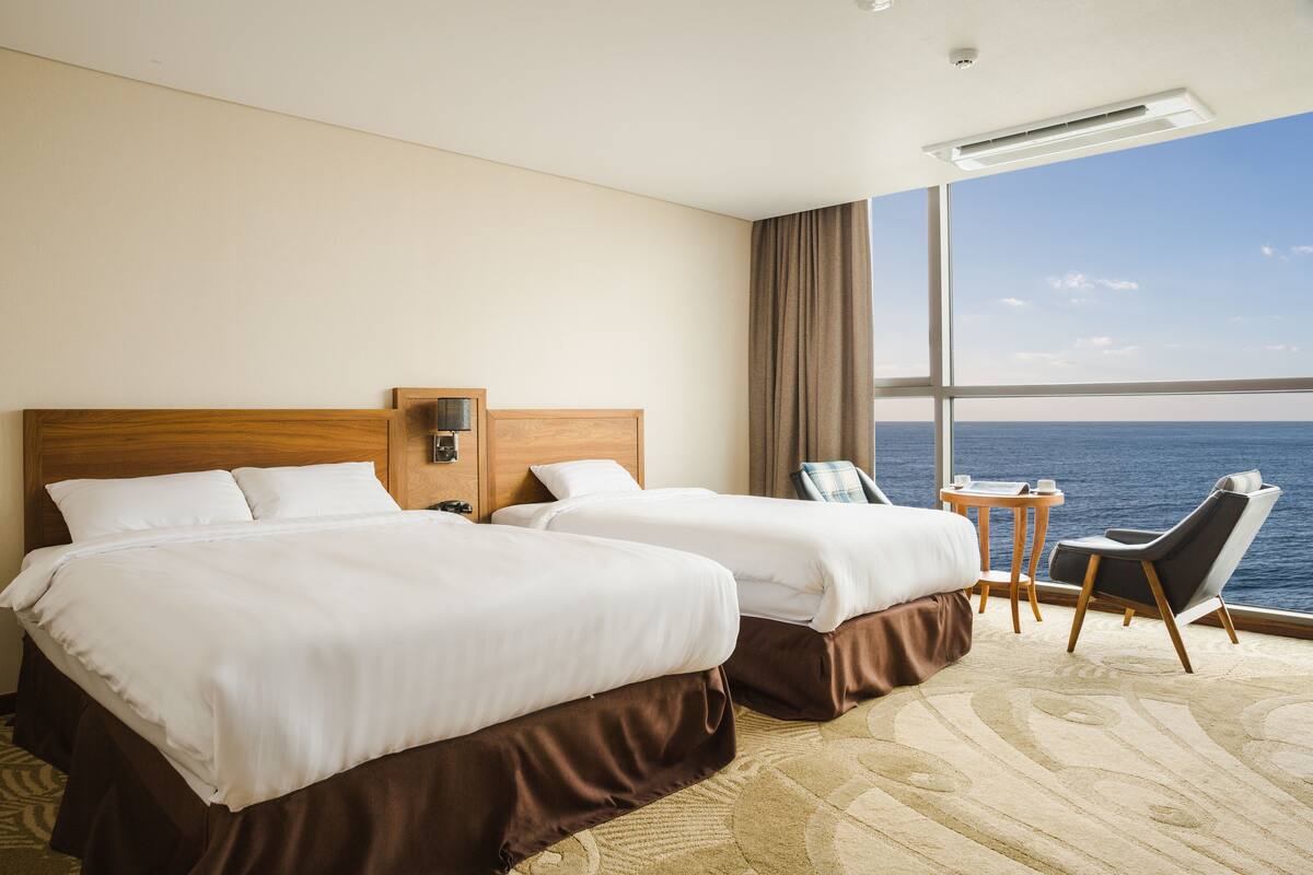 Ein Hotelzimmer mit zwei Betten, einem kleinen Tisch, einem Stuhl und Meerblick.