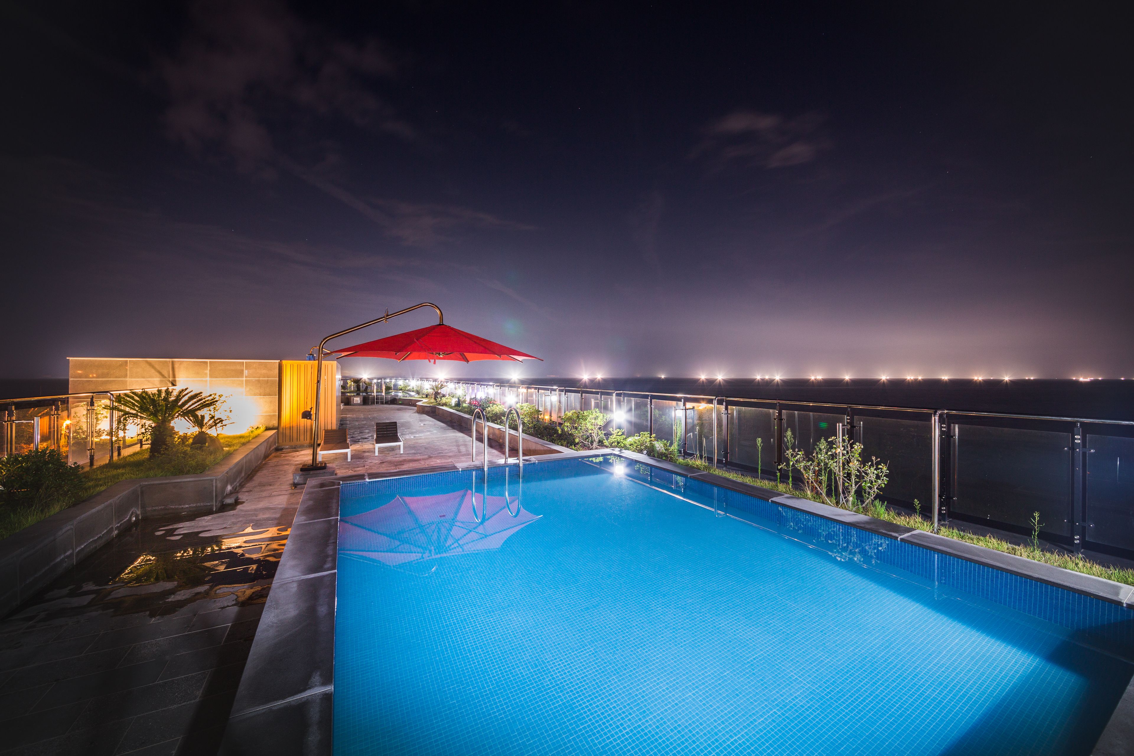 A swimming pool with a red canopy, surrounded by a deck and a railing, under a night sky.