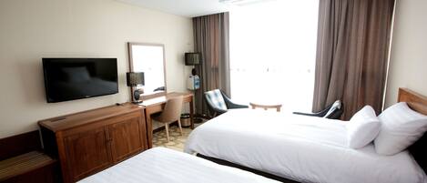 Ein Hotelzimmer mit zwei Betten, einem Schreibtisch, einem Stuhl, einem Fernseher und einem Fenster mit Vorhängen.