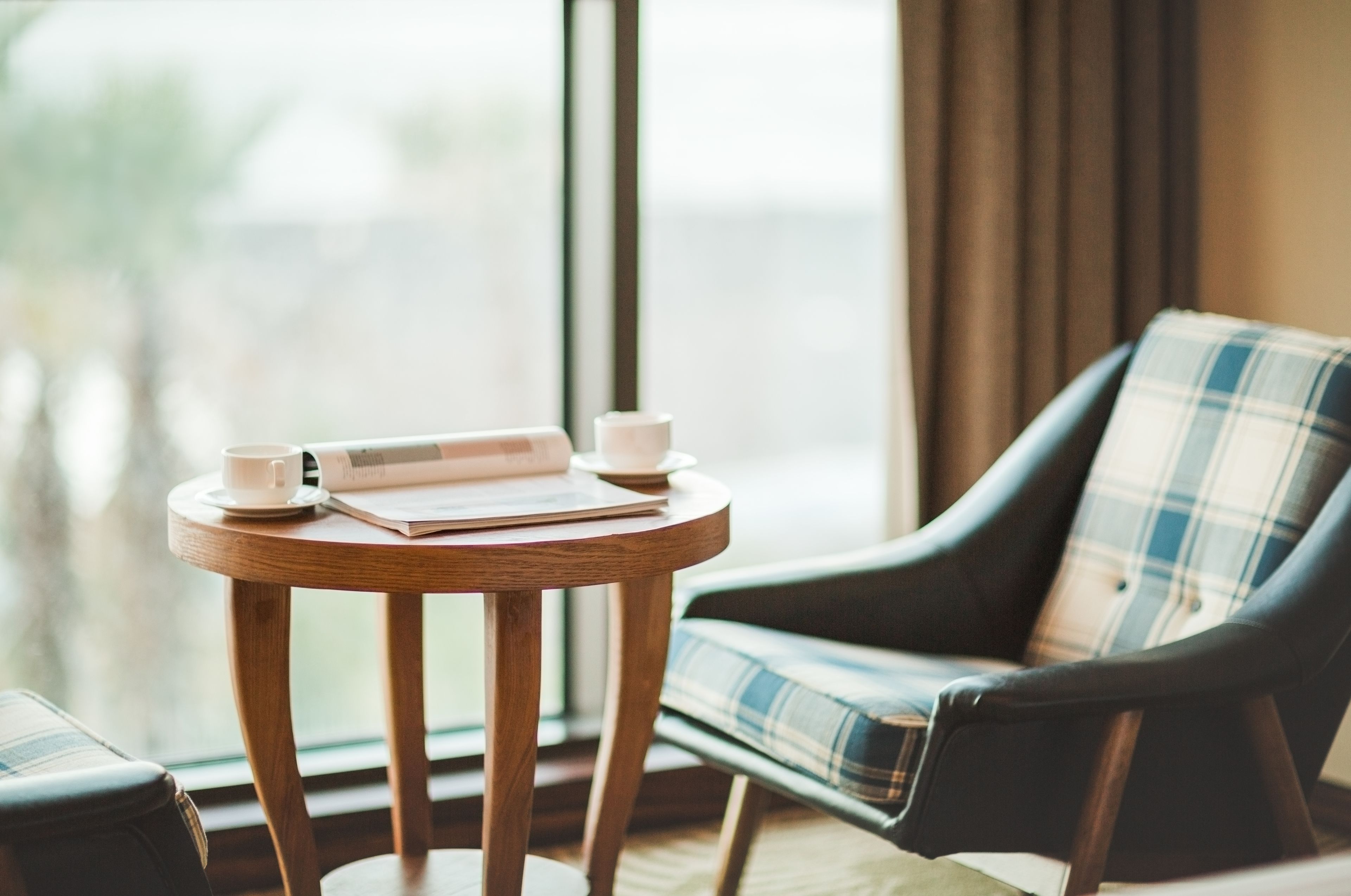 Un coin salon confortable avec une table ronde en bois, un canapé à carreaux et une fenêtre avec des rideaux.