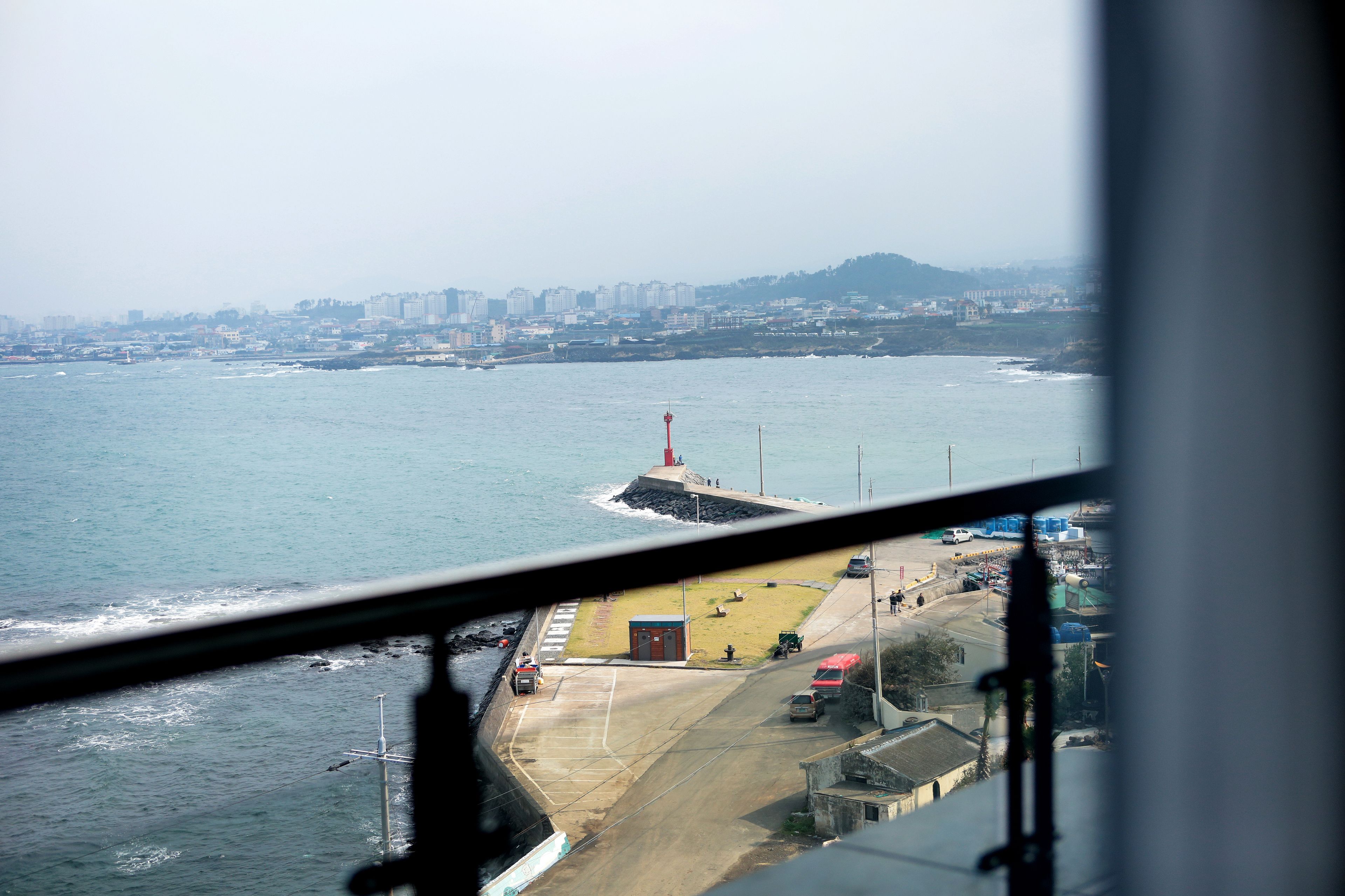 Un paysage urbain côtier avec un phare, une jetée et une route menant à un petit bâtiment.