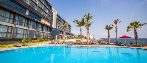 A hotel with a swimming pool, palm trees, and a view of the ocean.