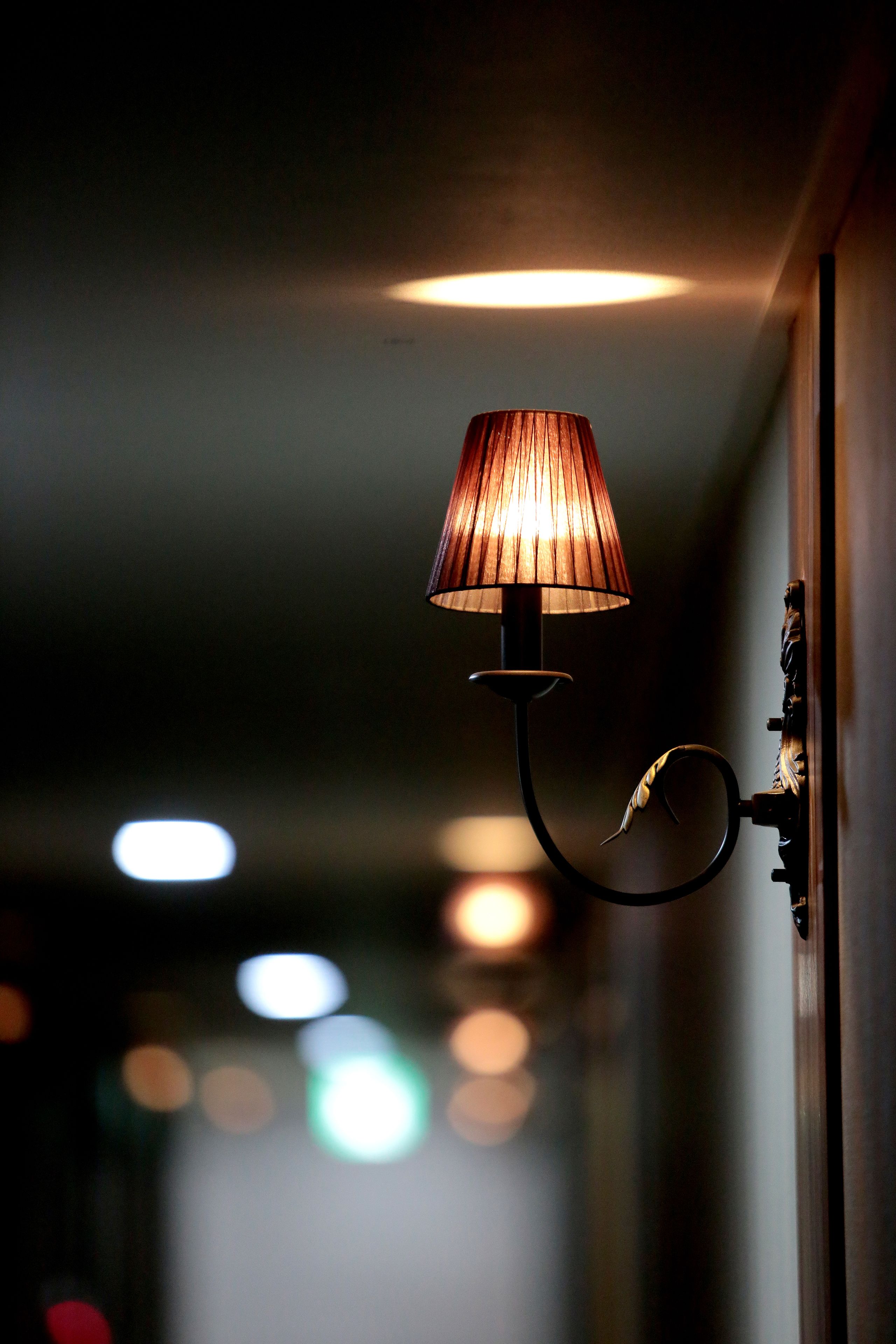 A wall-mounted lamp with a curved arm and a conical shade, positioned in a dimly lit hallway.