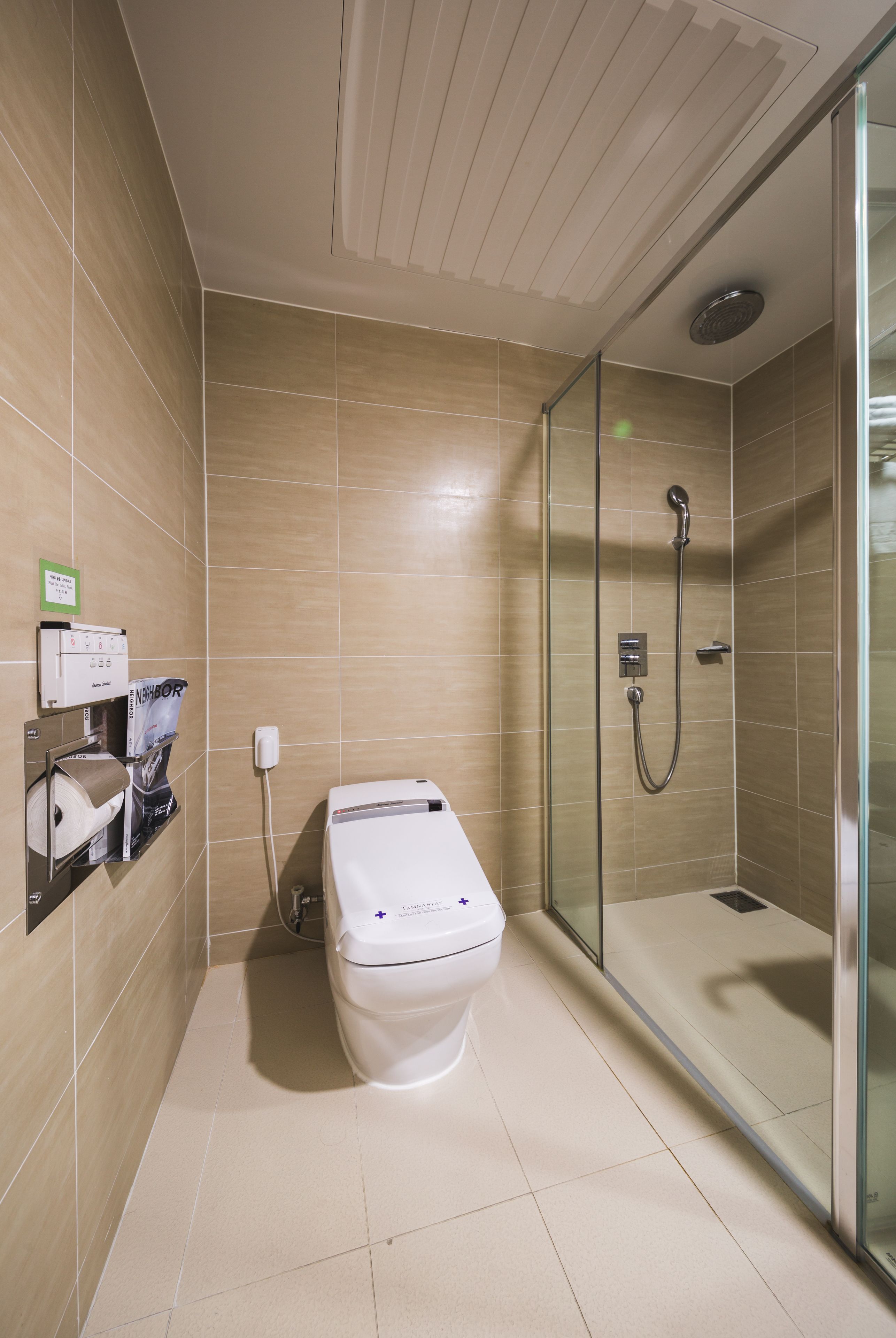 Un baño moderno con ducha envuelta en vidrio, inodoro y dispensador de toallas de papel.