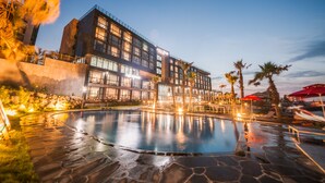 A modern hotel with a large pool, palm trees, and outdoor seating areas. - Tamna Stay Hotel Jeju (Jeju City)
