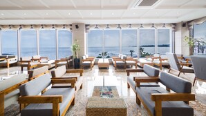 A spacious lounge with rows of wooden and upholstered seating, large windows offering a view of the sea, and a polished marble floor. - Tamna Stay Hotel Jeju (Jeju City)