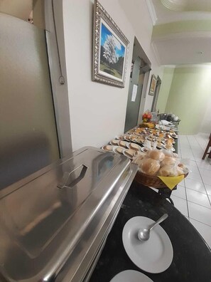 A buffet setup with various food items and a large serving tray. - Hotel Ipê (Guarulhos)