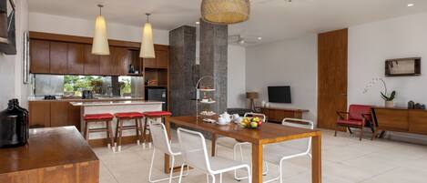 A modern kitchen with a dining area, white chairs, and a wooden table.