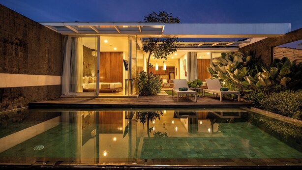 A modern house with a glass-enclosed patio, a swimming pool, and a well-lit interior.