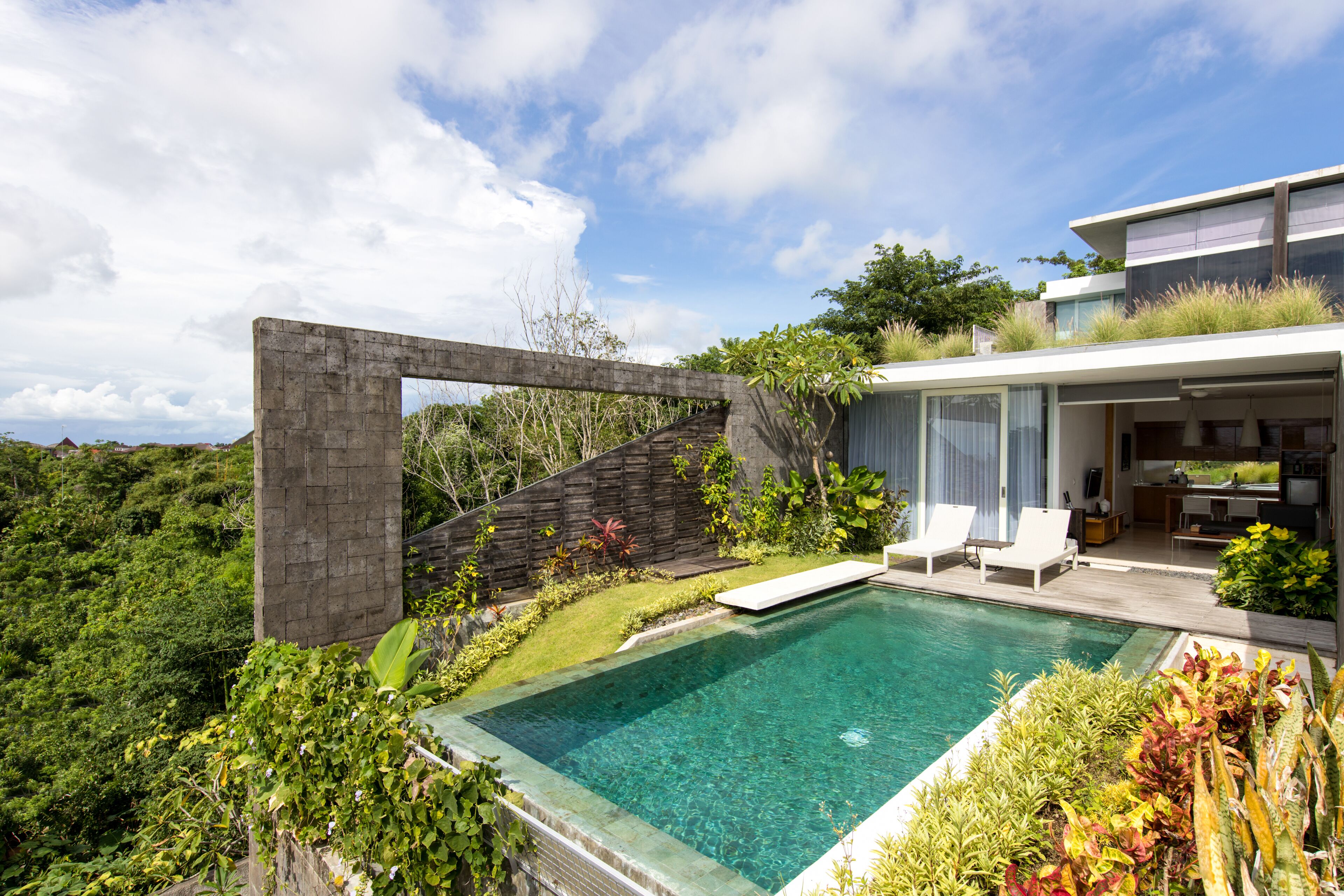 A modern house with a swimming pool, a patio with lounge chairs, and a view of the surrounding greenery.