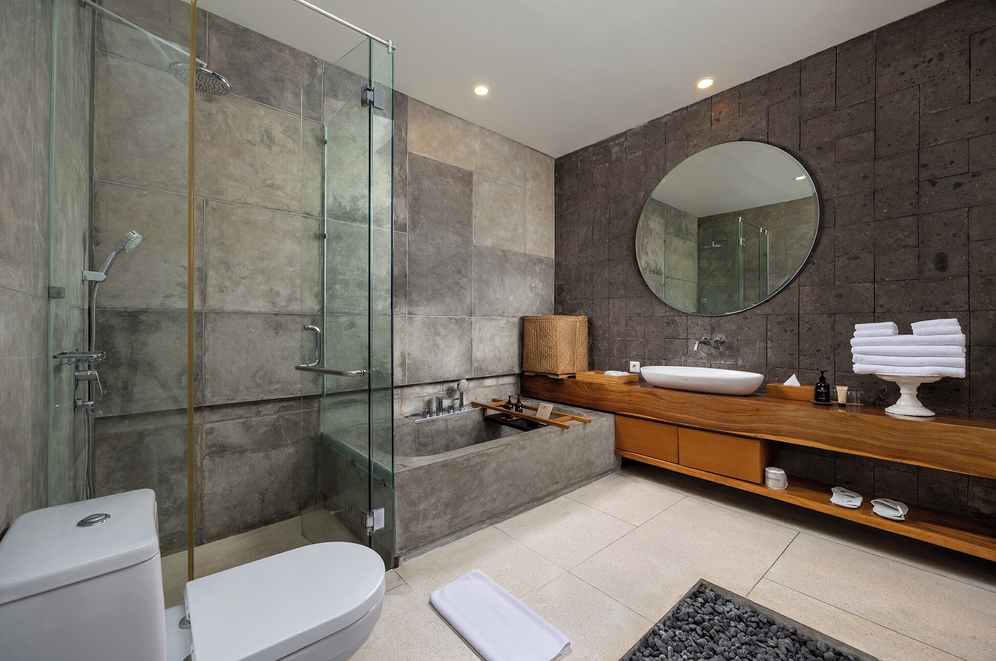 A modern bathroom with a glass shower enclosure, a white toilet, a freestanding bathtub, and a wooden vanity with a round mirror.