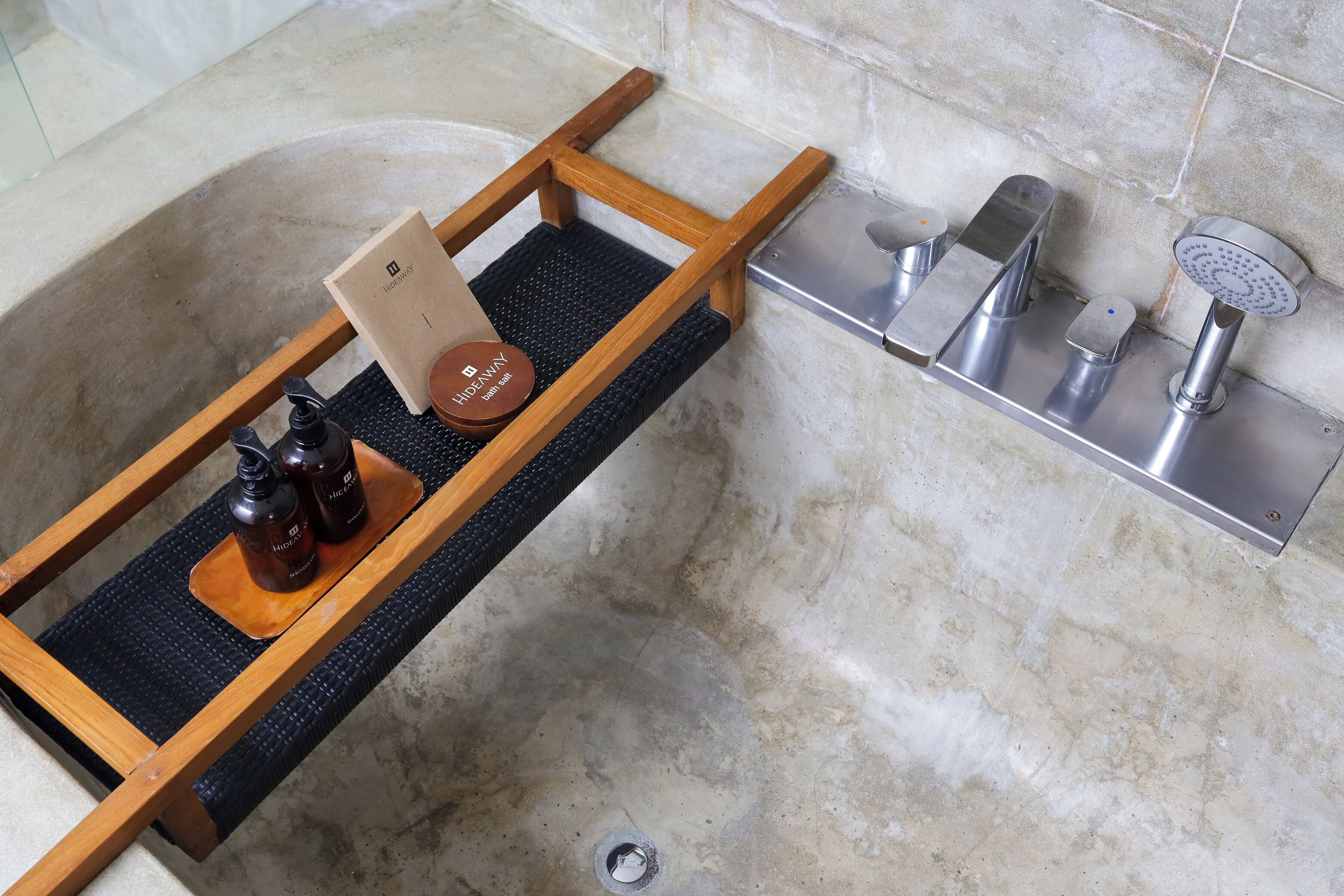 A bathroom with a wooden shelf holding a bath salt container, a bottle, and a card.