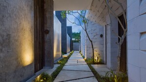A narrow, illuminated pathway flanked by modern buildings with geometric patterns and a small tree.