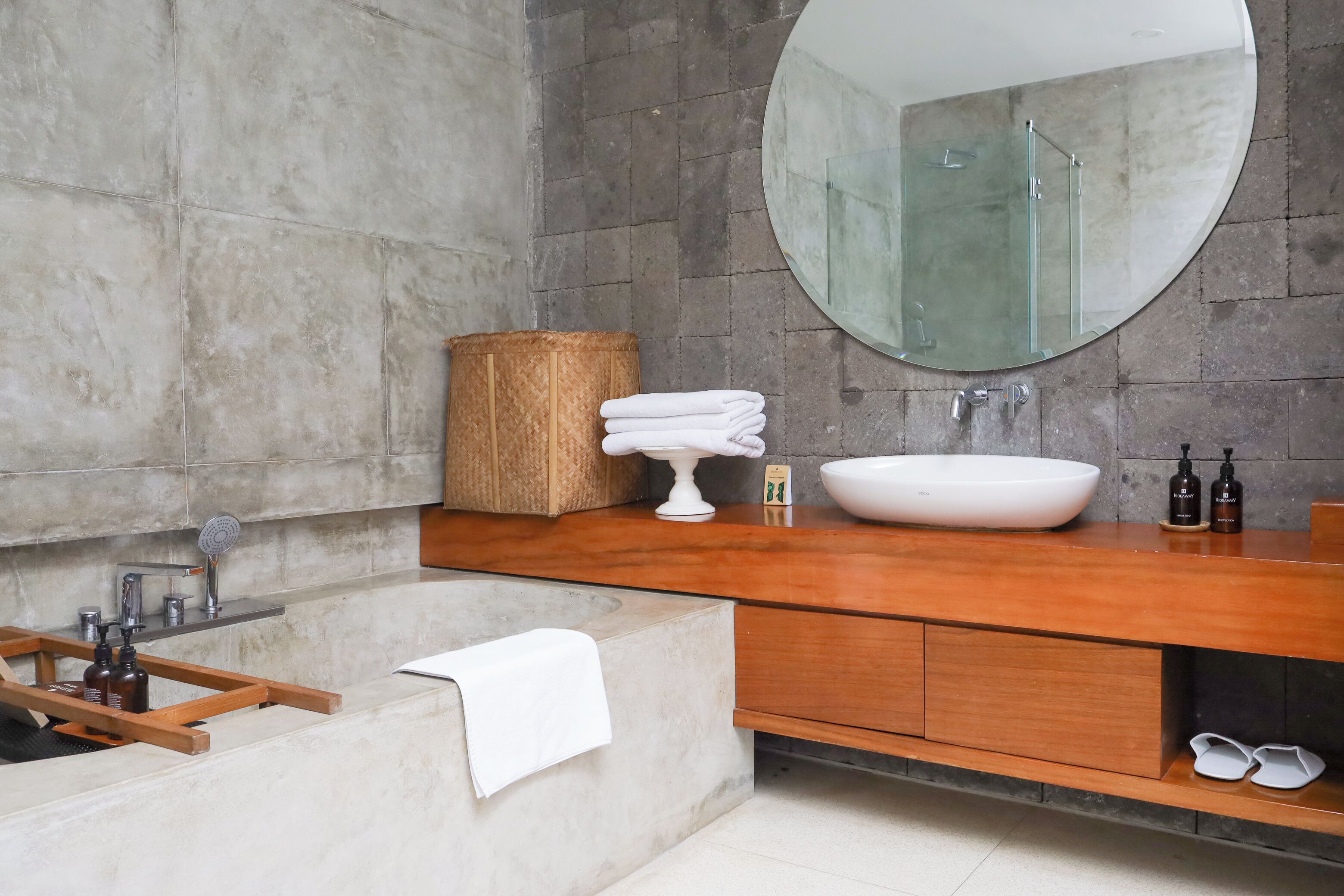 A modern bathroom with a large bathtub, a round mirror, a wooden vanity, and a large mirror above the sink.