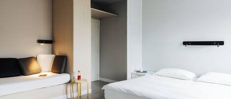 Una habitación de hotel moderna con cama, sofá, una mesita y un armario.