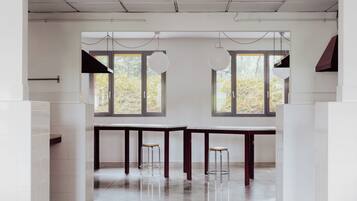 A modern kitchen with white tiled walls, a large window with a view of trees, and two hanging light fixtures.